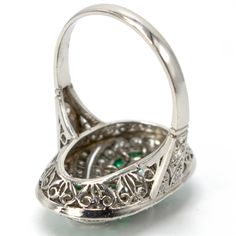 This jaw dropping ring, an Art Deco piece of art likely made in the 1920s, is made of platinum and features two central bezel set diamonds ensconced by an infinity-style figure eight channel of square cut emeralds. The rest of the ring's top contains multiple angular swirls of diamonds that are separated by pierced cut-outs, giving a palpable sense of motion to the piece. The shoulders are beautifully pierced and the undercarriage—or gallery—is ornately filigreed. Metal: Platinum Main Stones: 2 Platinum Oval Emerald Ring With 17 Jewels, Oval Platinum Emerald Ring With 17 Jewels, Platinum Emerald Ring In White Gold, Art Deco Emerald Ring In Platinum, Art Deco Platinum Emerald Ring, Oval Hallmarked Emerald Ring In Platinum, Hallmarked Oval Emerald Ring In Platinum, Art Deco Emerald Ring With Platinum, White Gold Oval Emerald Ring Art Deco Style