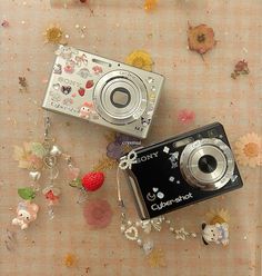 two cameras sitting next to each other on a table covered with flowers and beads,