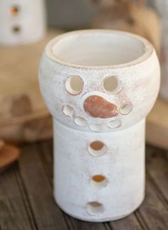 a white vase sitting on top of a wooden table with holes in it's face