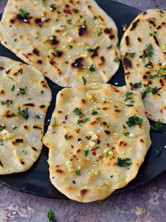 four flat breads on a black plate with parsley