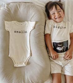 a little boy laying on top of a bed next to a baby bodysuit and pillow