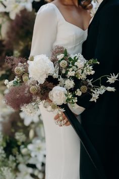 a bride and groom standing next to each other in front of white flowers on the wall