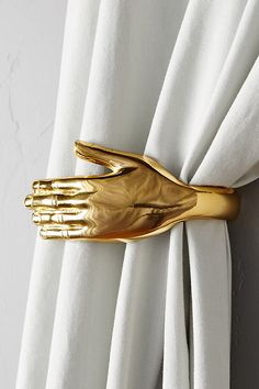 a gold hand napkin holder is hanging on a white drapeed curtain with two hands