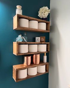 three wooden shelves with jars and candles on them against a blue wall in a bathroom