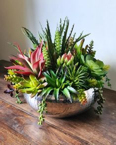 a metal bowl filled with lots of green and red flowers on top of a wooden table