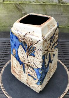 a blue and white square vase sitting on top of a wooden table next to a fence