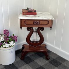 a small table with some books on it next to a potted plant and flowers