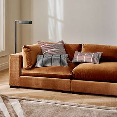 a brown couch with pillows on it in front of a white wall and floor lamp