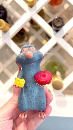 a hand holding a toy mouse with a doughnut in it's mouth and wine bottles behind it