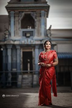 a woman in a red sari posing for the camera with an old building behind her