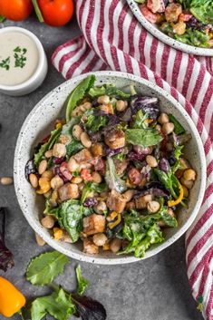 two bowls filled with salad next to tomatoes and lettuce on a tablecloth