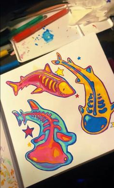 two colorful fish stickers sitting on top of a white paper next to paintbrushes