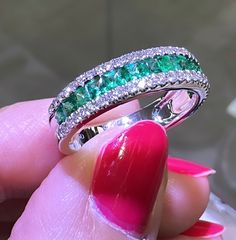 a woman's hand holding a ring with emeralds and diamonds on it,