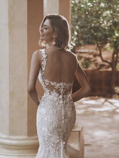 a woman in a white wedding dress standing outside with her back turned to the camera