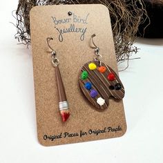 a pair of wooden earrings with paintbrushes and acrylic colors on them