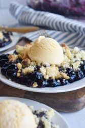 blueberry cobbler with ice cream on top sitting on a wooden table next to other desserts