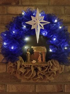 a nativity wreath with blue lights and a star hanging from the top on a brick wall