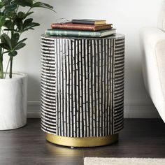 a black and white side table with books on it next to a potted plant