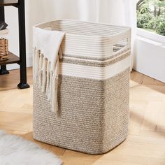 a white and beige basket sitting on top of a wooden floor next to a window