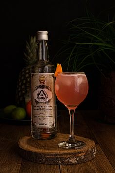 a bottle of alcohol next to a glass filled with pink liquid and an orange slice