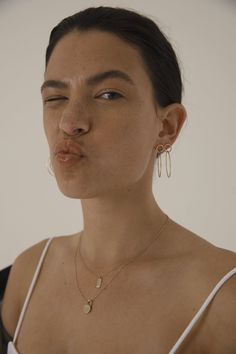 a woman with her nose open wearing gold earrings and a white tank top is posing for the camera