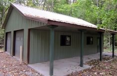 a small green building sitting in the middle of a forest with lots of leaves on the ground