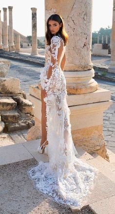 a woman standing in front of columns wearing a white dress with sheer lace on it