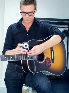 a man sitting down playing an acoustic guitar