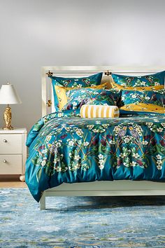 a bed with blue and yellow comforters on top of it next to a night stand