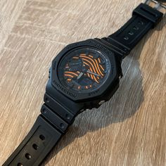 "A customized Casio G-Shock GA-2110 altered with a new dial featuring the print named \"Grain\" in black and orange. The minimalistic and subtle alterations give a whole new look to the rugged and popular watch from Casio. This product uses a brand new authentic Casio G-Shock GA-2110, the watch comes with the original box and papers. This is a handmade product, slight variations may apply. Different colours are available, more designs on the way but inquiries are always possible through chat. Case size (L× W× H) 48.5 × 45.4 × 11.8 mm Case and bezel material Case / bezel material: Carbon / Resin Band Resin Band Disclaimer: - This brand has no affiliation with Casio" Black Sports Watch Shock Resistant, Black Shock Resistant Watches For Sports, Black Shock Resistant Sports Watch, Black Watch With Stopwatch For Streetwear, Black Stopwatch Watch For Streetwear, Black Streetwear Watch With Stopwatch, Black Casual Watch For Streetwear, Black Casual Streetwear Watch, Casual Black Streetwear Watch