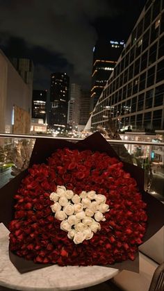 a bouquet of roses in the shape of a heart on top of a table next to a cityscape