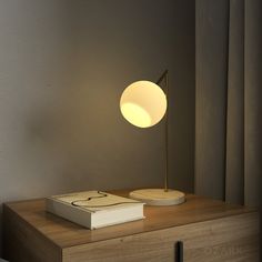 a table lamp sitting on top of a wooden dresser next to a book and window