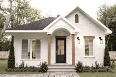 a small white house with black door and brick walkway leading up to the front door