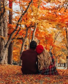 two people sitting on the ground in front of trees with leaves all around them and one person is holding his head back