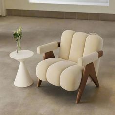 a white chair and table with a vase on the floor in front of it next to a window