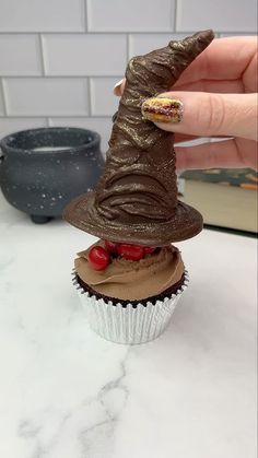 a cupcake with chocolate frosting and a witches hat on top is being held up by a woman's hand