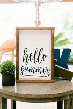 a hello summer sign sitting on top of a table next to a potted plant