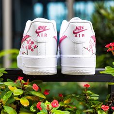 a pair of white nike air force sneakers sitting on top of a wooden bench surrounded by flowers