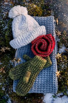 two knitted hats and scarfs laying on top of snow covered ground