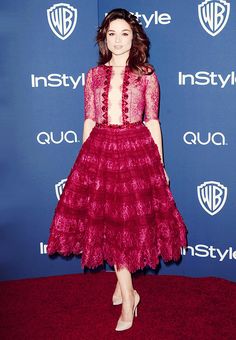 a woman in a red dress standing on a red carpet at an instyle event