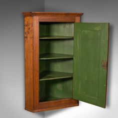 an old wooden cabinet with green paint on the door and shelves in front of it