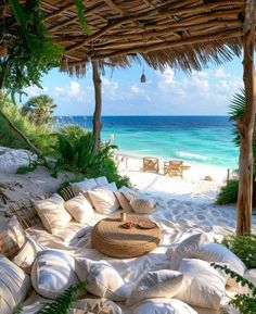 an outdoor seating area on the beach with pillows and straw umbrellas over looking the ocean