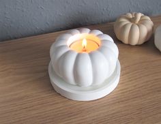 a small white candle holder sitting on top of a wooden table next to two pumpkins