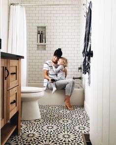 a man and woman sitting on top of a toilet next to each other in a bathroom