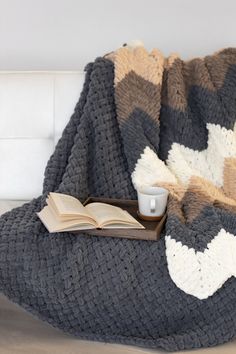 a coffee cup and book on a couch with a crocheted blanket draped over it