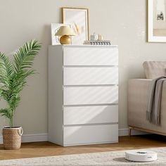 a white chest of drawers sitting in a living room next to a couch and potted plant