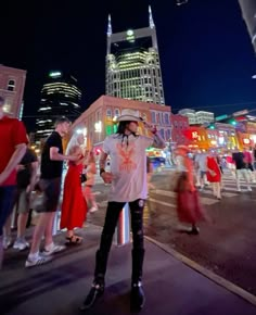 a woman standing in the middle of a street at night with people walking around her