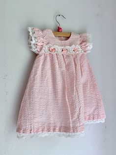 "This dress by Bonnie Baby has so many fancy details.  Peach gingham, lace details on the sleeves and hem, ribbon flowers. Marked 18 months, this measures 10\" flat across the chest and 19\" in total length.  This is in excellent condition." Sweet Gingham Cotton Dress, Sweet Gingham Dress With Ruffles, Pink Lace Dresses With Crochet Trim, Pink Lace Dress With Crochet Trim, Cute Peach Cotton Dress, Cute Gingham Dresses With Lace Trim, Pink Cotton Dress For Tea Party, Pink Cotton Dress With Crochet Trim, Cotton Gingham Dress With Lace Trim