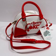 The Bag Is Made Of High-Quality Faux Leather And Nylon, With A Canvas Lining For Added Comfort. It Also Comes With A Bag Charm And Other Strap For Added Versatility. A Gorgeous White Exterior And Red Faux Leather Handles, This Bag Is Sure To Turn Heads. It Features A Zip Closure And An Adjustable Strap For Your Convenience. The Cherry Coke Pattern And London Theme Make This Bag A Must-Have For Any Coca-Cola Fan Or Collector. Retro Crossbody Satchel For Errands, Retro Satchel Bag For Errands, Red Handheld School Bag, Retro Red Crossbody Bag, Red Retro Crossbody Bag, Retro White Crossbody Satchel, Retro White Satchel With Adjustable Strap, Retro White Shoulder Bag For School, Retro Shoulder Bag With Zipper Closure