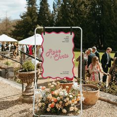 a sign that is sitting on the ground near some plants and people in the background